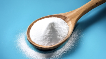 Baking soda in wooden spoon isolated on light blue background