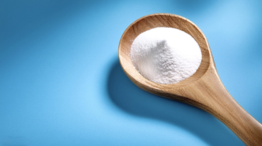 Baking soda in wooden spoon isolated on light blue background
