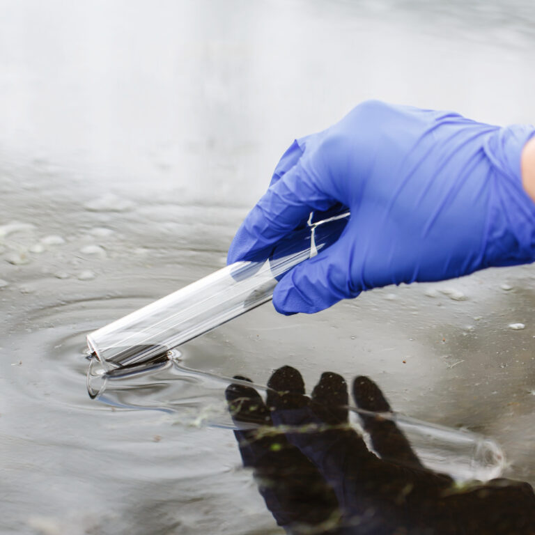 Researcher holds a test tube with water in a hand in blue glove