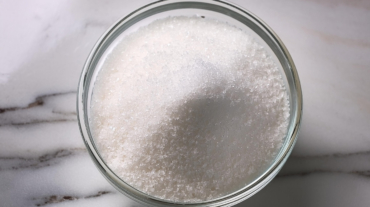 Granulated sugar in a glass bowl on a marble background