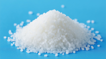 Pile of white salt on a blue surface. The salt is white and has a grainy texture