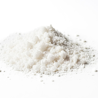 Close-up shot of white salt crystals on white background. The salt crystals are piled up in a small heap and are illuminated by bright light. The background is blurred and out of focus.